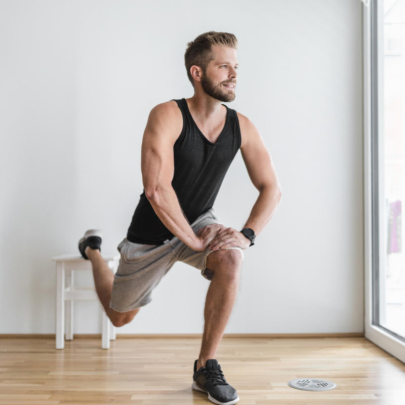 Man performing a leg stretch in a bright room with large windows.